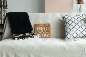 a wooden letterboard with the phrase "don't let perfect stand in the way of progress" on a sofa in a natural light photography studio